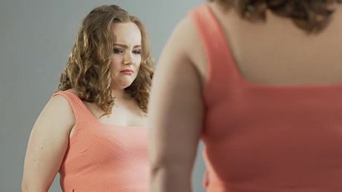 体重超重的女性带着自我厌恶看着镜子里的倒影