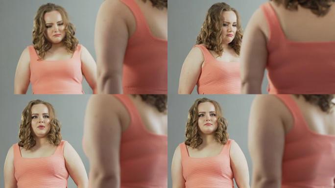 体重超重的女性带着自我厌恶看着镜子里的倒影