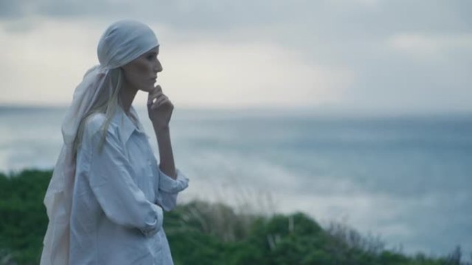 美丽的女人，围巾遮住头发，站在海边的悬崖上