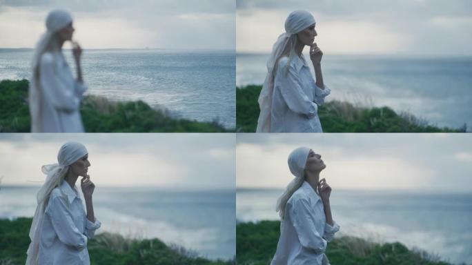 美丽的女人，围巾遮住头发，站在海边的悬崖上