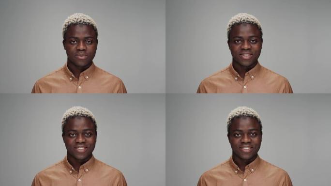 彩色摄影棚拍摄的年轻黑人男子看着相机的肖像。成年非洲男孩独自在灰色背景特写中孤立。非裔美国人张开美丽