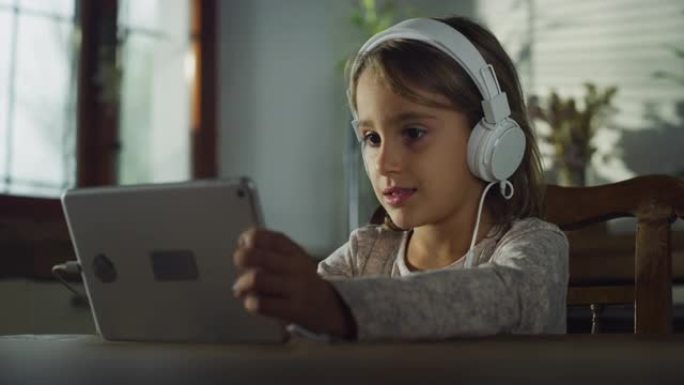 真实的小女孩在数字平板电脑上观看孩子们的表演，通过耳机收听。厨房里的女学生在享受周末的早晨，使用技术