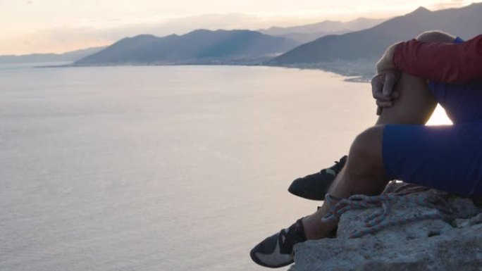 成熟的男性攀岩者在岩石山顶上放松，俯瞰大海