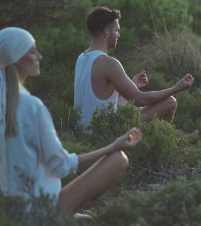 两个朋友坐在海边的草崖上放松身心。莲花姿势冥想和练习健康垂直视频