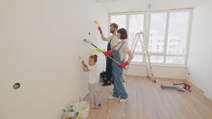 公寓里的维修。幸福的家庭。幸福的家庭母亲，父亲和孩子的女儿用油漆粉刷墙壁。年轻的父亲和母亲向孩子展示