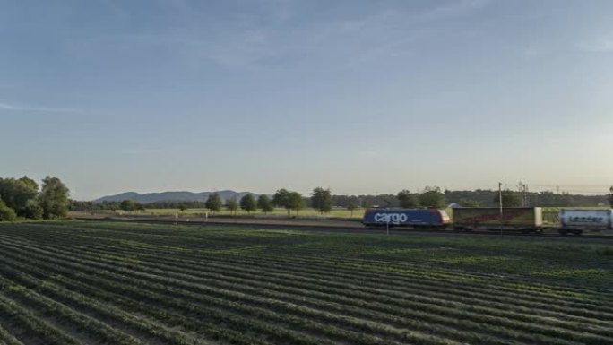 空中无人机拍摄了一列货运火车在日落时分穿过农田