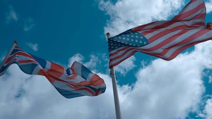 旗杆上的美国和英国国旗在蓝天下随风飘扬