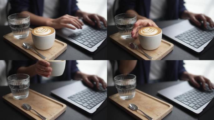 一名在笔记本电脑上工作的妇女喝了一口咖啡的特写镜头