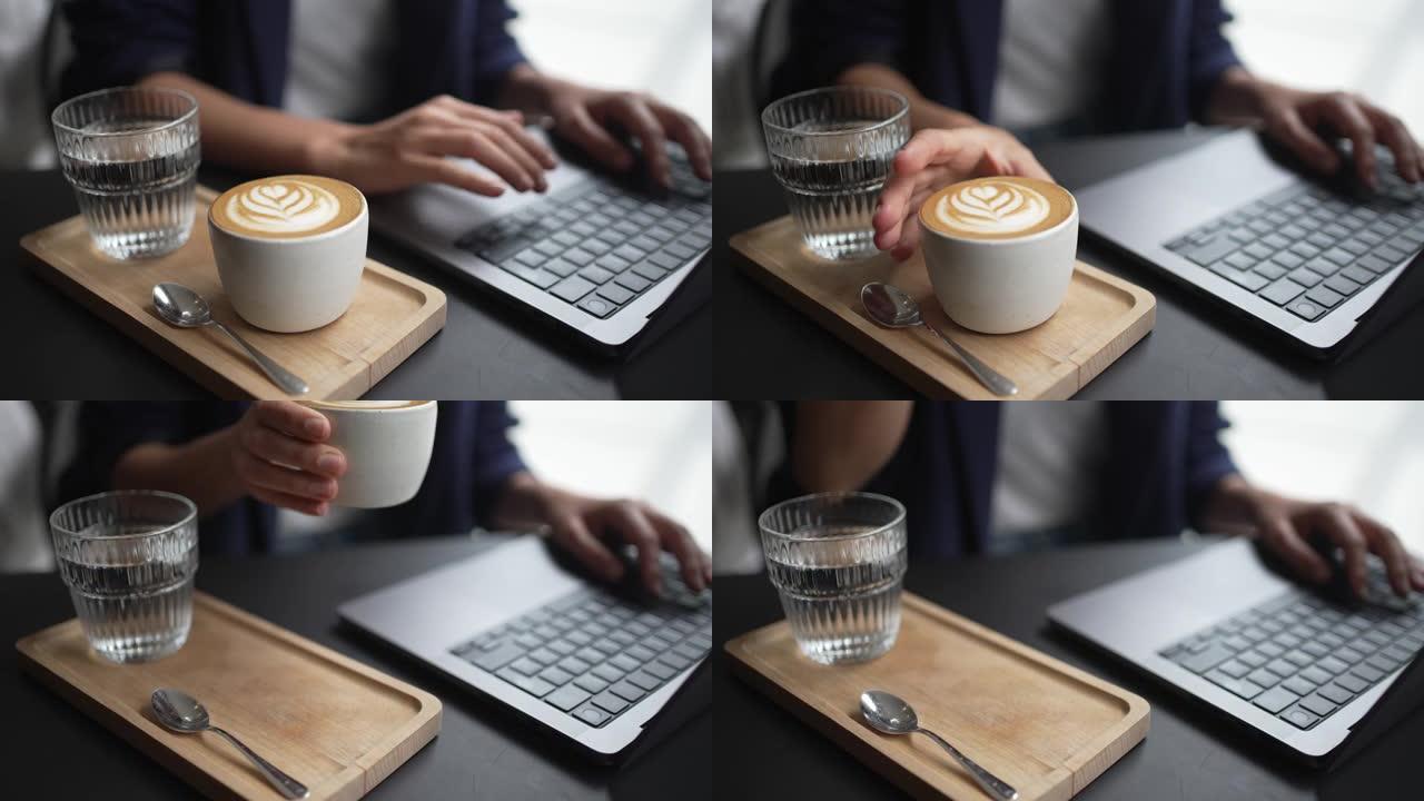 一名在笔记本电脑上工作的妇女喝了一口咖啡的特写镜头