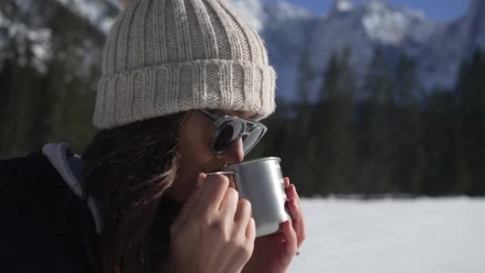 特写镜头，一名年轻女子从杯子里喝酒，欣赏雪山的景色