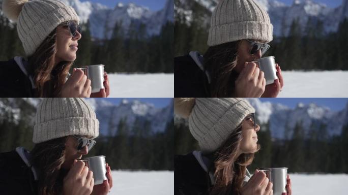 特写镜头，一名年轻女子从杯子里喝酒，欣赏雪山的景色