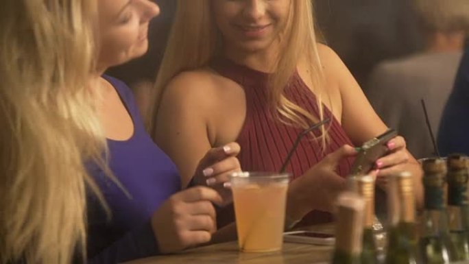 迷人的金发女郎在智能手机上观看视频，在酒吧聚会上玩得开心