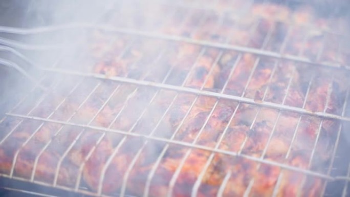 肉是在烟雾特写下烹饪的，视差。鸡翅在烤架上的网格中，相机运动平稳