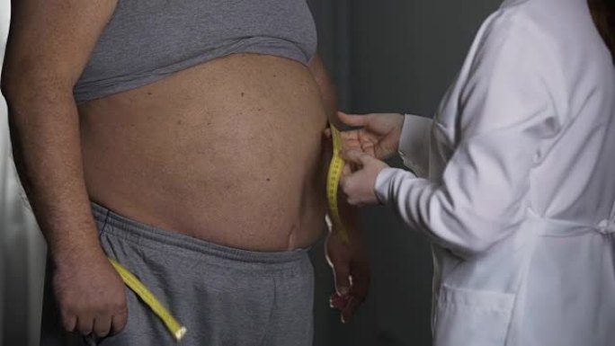 营养师测量超重男性患者的腰围，节食和肥胖