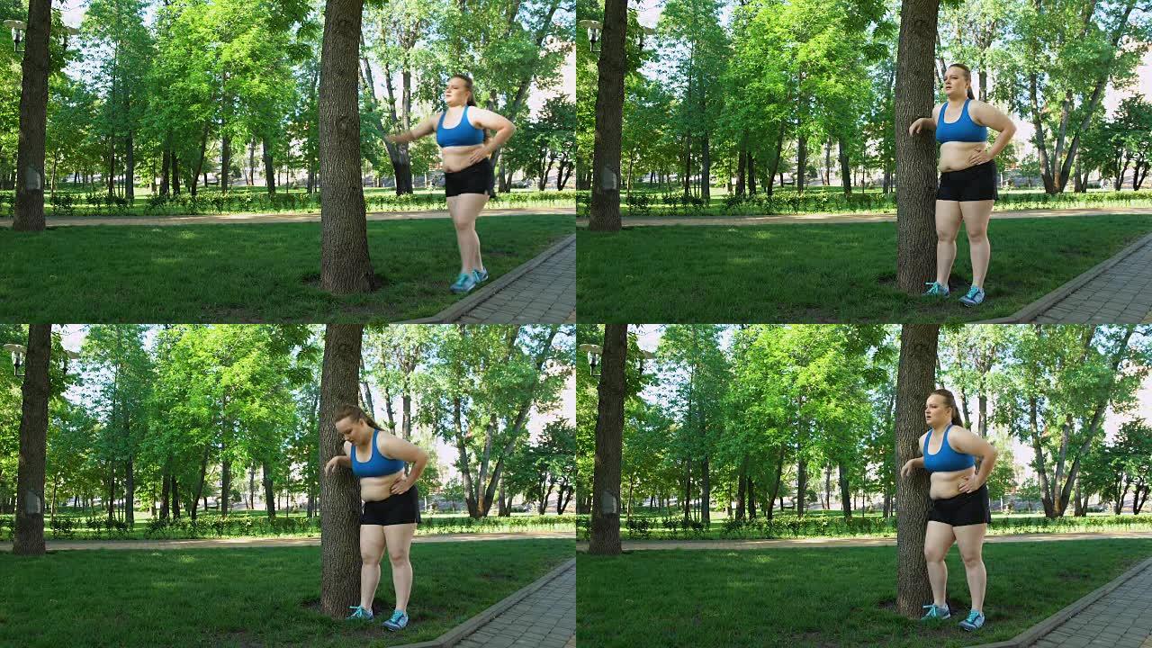 肥胖女孩慢跑后疲倦，靠在树上，在户外进行烦人的锻炼