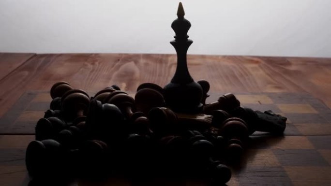 国际象棋黑皇后站在棋盘上，被其余的躺着的棋子包围着。棋盘游戏。摄像机沿着物体移动