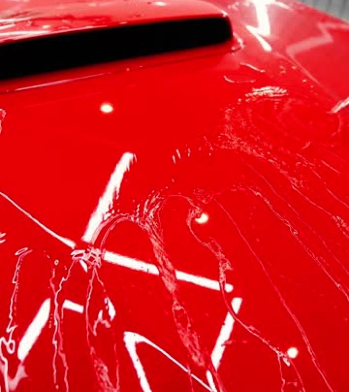 男子洗一辆红色汽车，在引擎盖上倒水。检查陶瓷防护涂层防雨层。洗车或汽车细节处理。垂直视频
