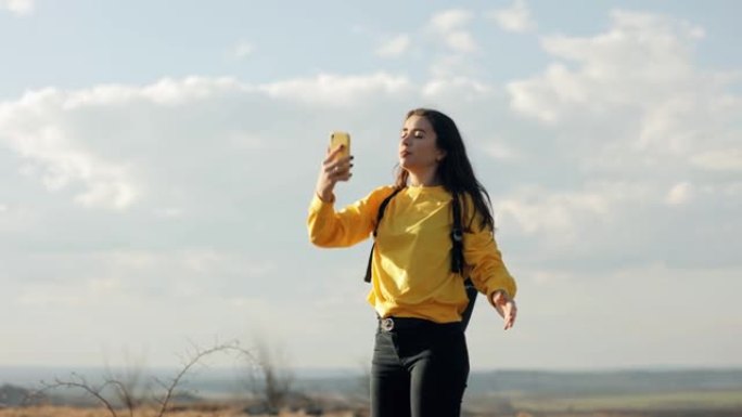 穿着黄色毛衣的女游客背着背包，试图在山上捕捉手机的信号，但没有信号，她很沮丧