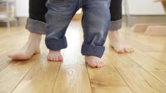 婴儿的脚在母亲抱着的木地板上行走