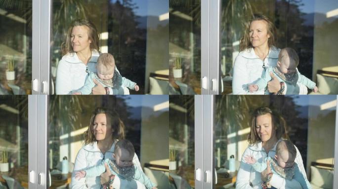 母亲怀抱的小婴儿在玻璃门后面望向日落