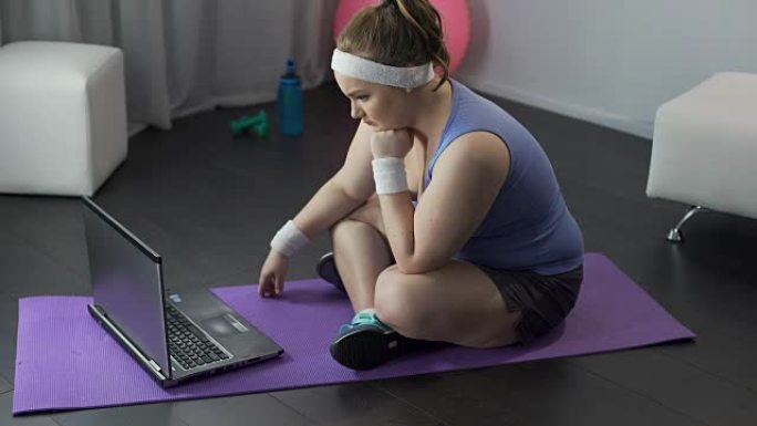 胖乎乎的女孩在笔记本电脑上紧张地阅读教练的锻炼和饮食计划
