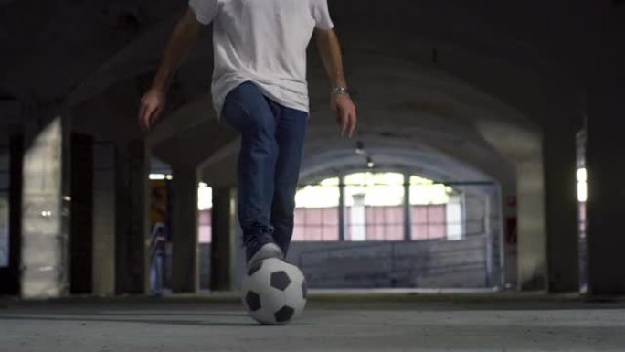 低角度，地面水平射击: 专注于有才华的年轻足球运动员的腿，熟练地玩弄球。男子在地下停车场展示他的自由