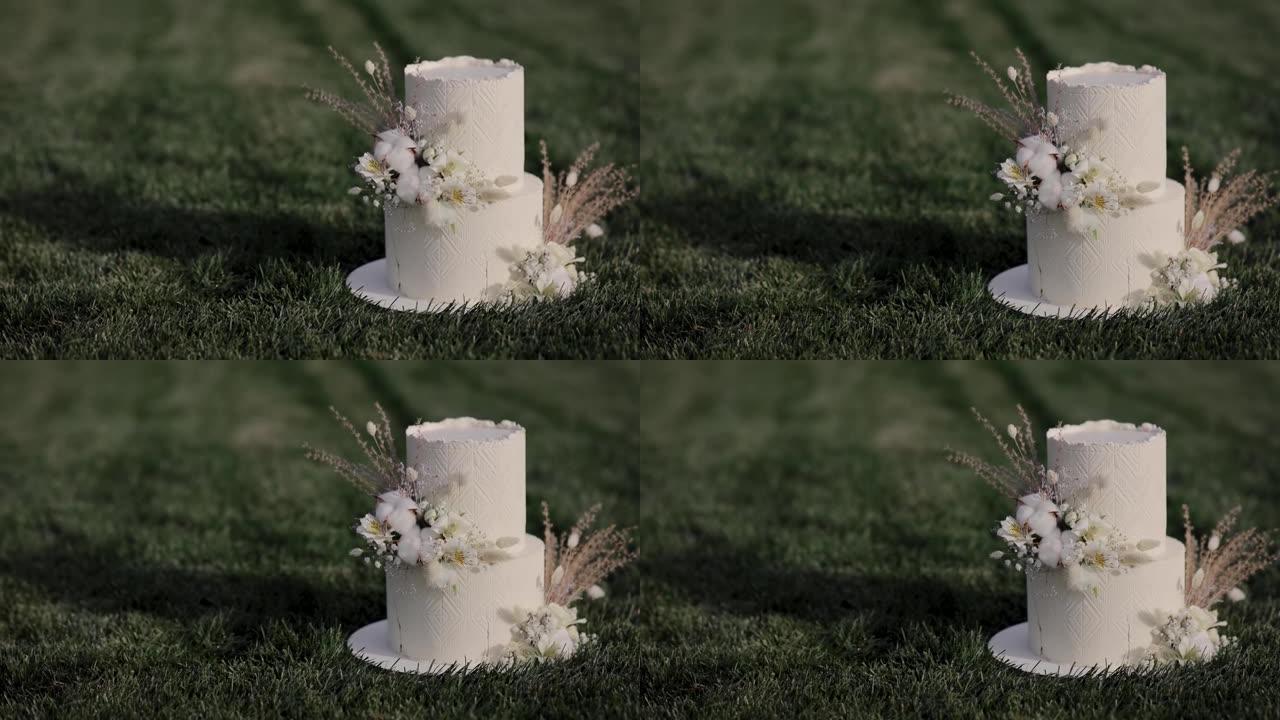 美味的两层婚礼蛋糕。白色婚礼蛋糕的特写，在波西米亚风格的糖衣上有干花的花卉装饰