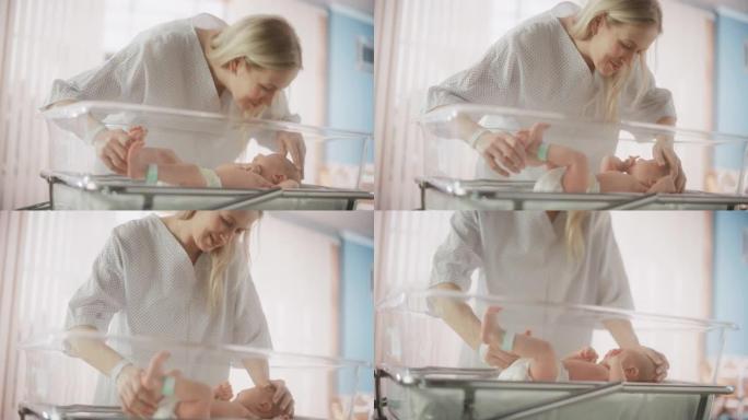 现代医院中母亲与新生婴儿联系的肖像。年轻女子在额头上亲吻她的孩子。婴儿躺在产科诊所的摇篮中