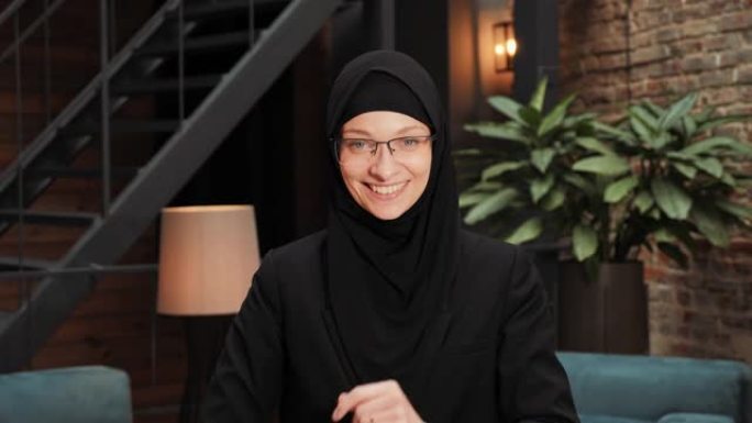 穿着黑色传统头巾的美丽漂亮阿拉伯穆斯林妇女的肖像直视镜头，在现代阁楼办公室微笑。微笑着的女性漂亮脸蛋