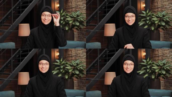 穿着黑色传统头巾的美丽漂亮阿拉伯穆斯林妇女的肖像直视镜头，在现代阁楼办公室微笑。微笑着的女性漂亮脸蛋