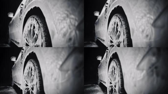 黑色电动SUV的商业慢动作镜头，上面覆盖着洗手液和泡沫。泡沫从汽车的后挡泥板滴落到家用汽车的轮胎和轮