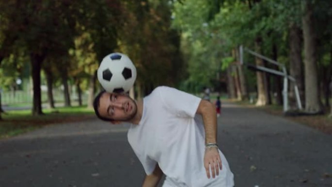 才华横溢的年轻足球运动员熟练地玩弄球，在阳光明媚的日子里在公共场合表演。时髦的男人在公园里炫耀自己的