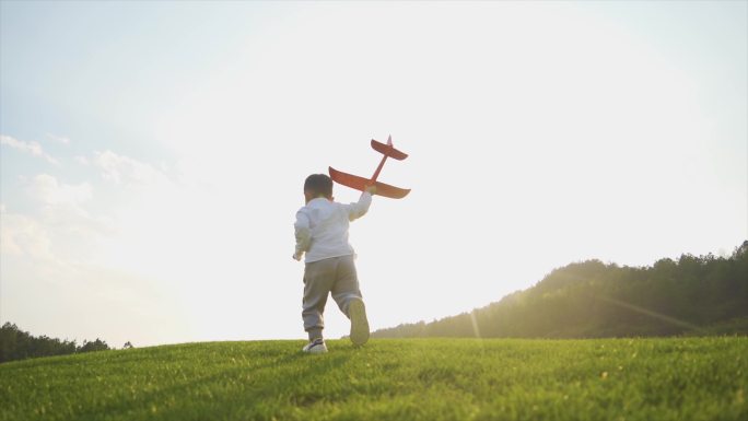 小男孩草地逆光奔跑小孩背影举起飞机模型