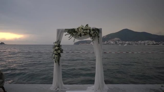 一排排白色椅子站在海边码头的婚礼拱门前