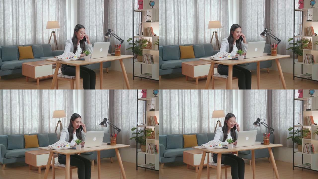 亚洲女鞋设计师在家中使用笔记本电脑时在智能手机上聊天
