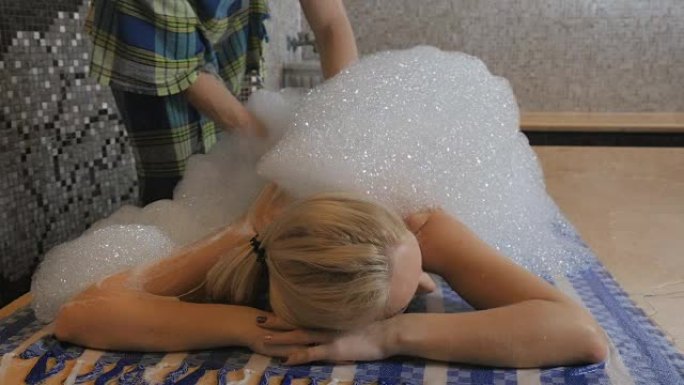 专业的按摩师在浴缸中用泡沫按摩妇女的背部