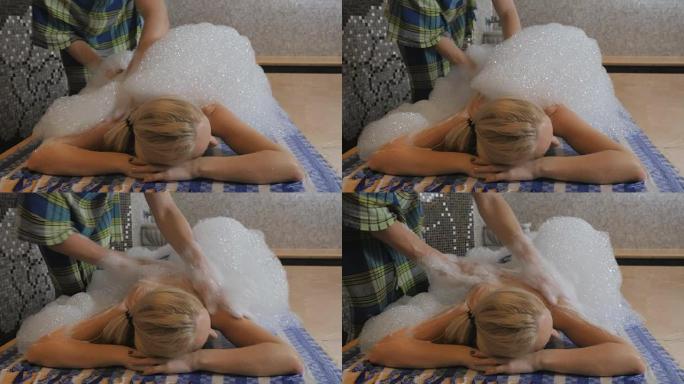 专业的按摩师在浴缸中用泡沫按摩妇女的背部