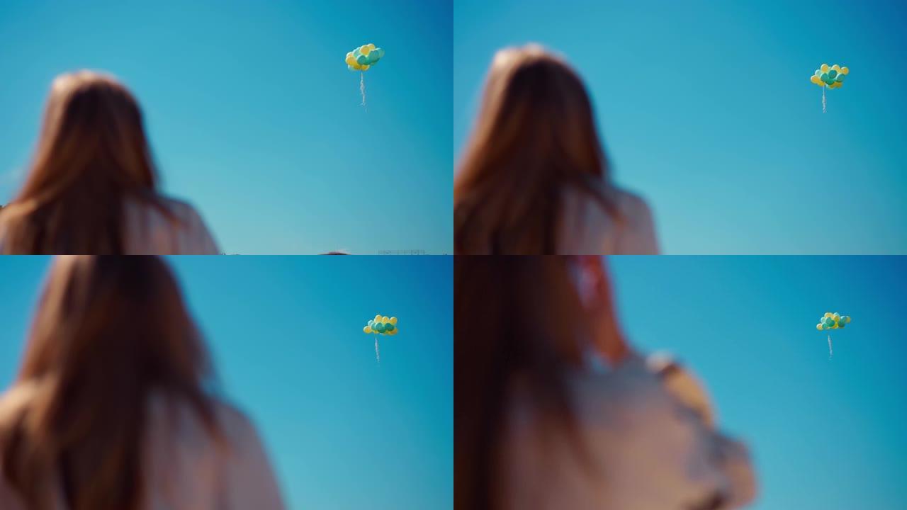 宽阔的蓝色黄色气球在无云的天空上飞行，左边是模糊的少女。春夏日里阳光装饰，户外自信的青少年。