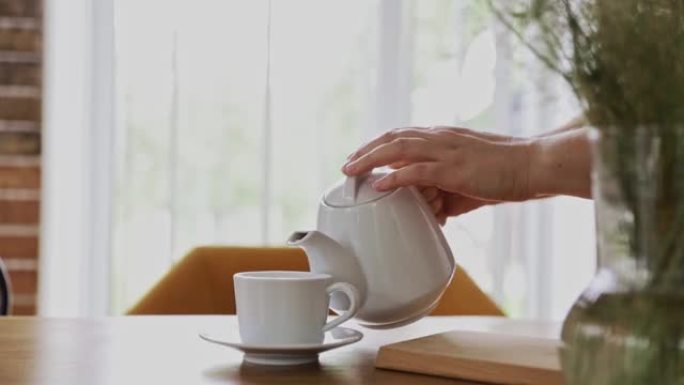 手正在室内将热饮从茶壶倒入茶杯或茶杯