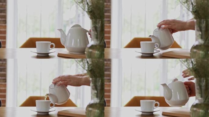 手正在室内将热饮从茶壶倒入茶杯或茶杯