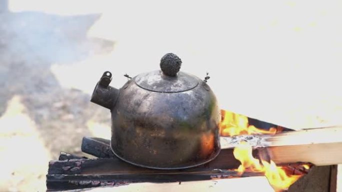 战役中的水壶着火了。徒步茶会。烟灰黑的水壶在篝火上沸腾。