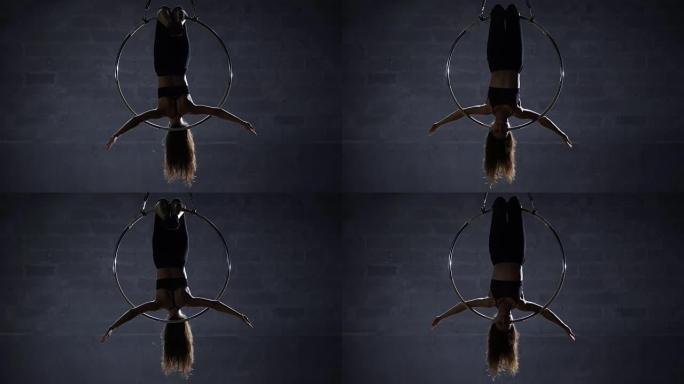 漂亮的体操运动员倒挂在空中吊环上