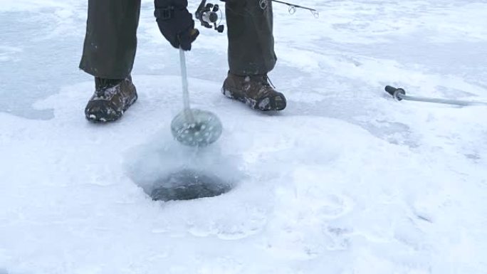 男子在冰冻的湖上挖出冰钓洞