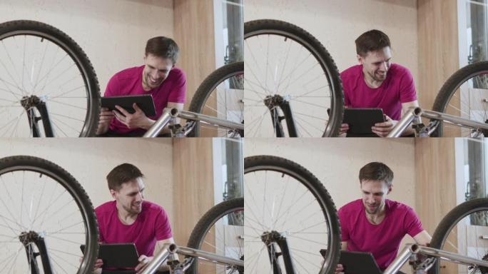 带平板电脑的人坐在自行车附近，踏板被拆下。快乐的家伙看着自行车。