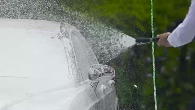 男子使用专业洗车设备在汽车上喷洒泡沫或水