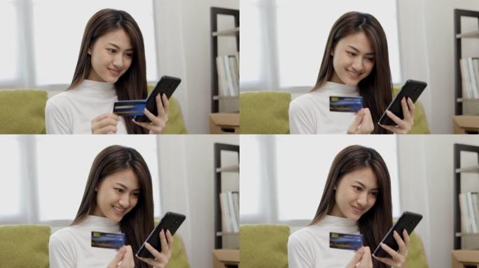 网上购物。年轻的亚洲少女将信用卡的序列号输入智能手机进行购物付款。在家在线送货购买商品。微笑的女性感