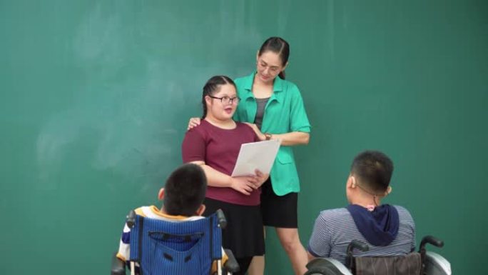 青少年唐氏综合症女孩练习演讲，在轮椅上与残疾学童小组一起阅读纸上演讲，亚洲美女老师站在课堂上鼓励他们