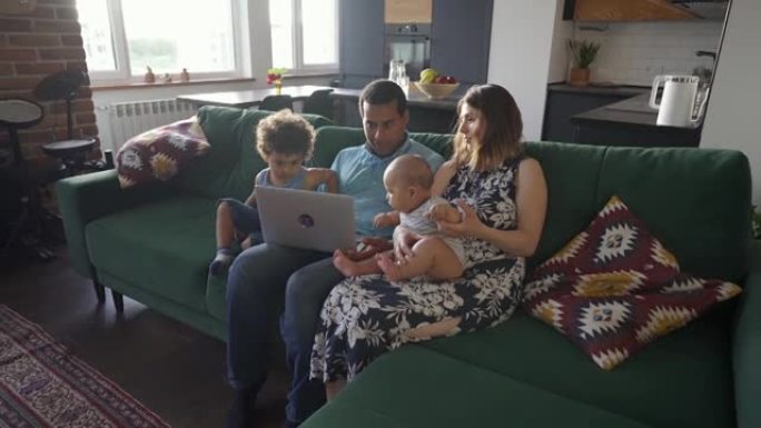 有两个孩子的混血家庭看着坐在家里沙发上的笔记本电脑屏幕