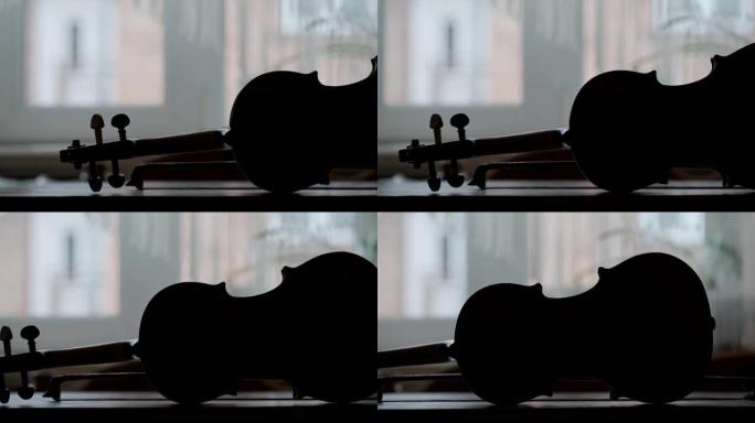 木制桌子上的古董小提琴的轮廓，弓和背景中的窗户。戏剧性的音乐情绪。