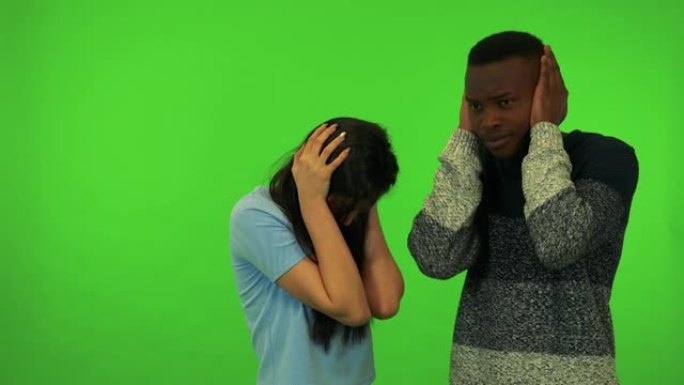 一名年轻的亚洲妇女和一名年轻的黑人男子从一个令人不快的声音-绿色屏幕工作室遮住耳朵